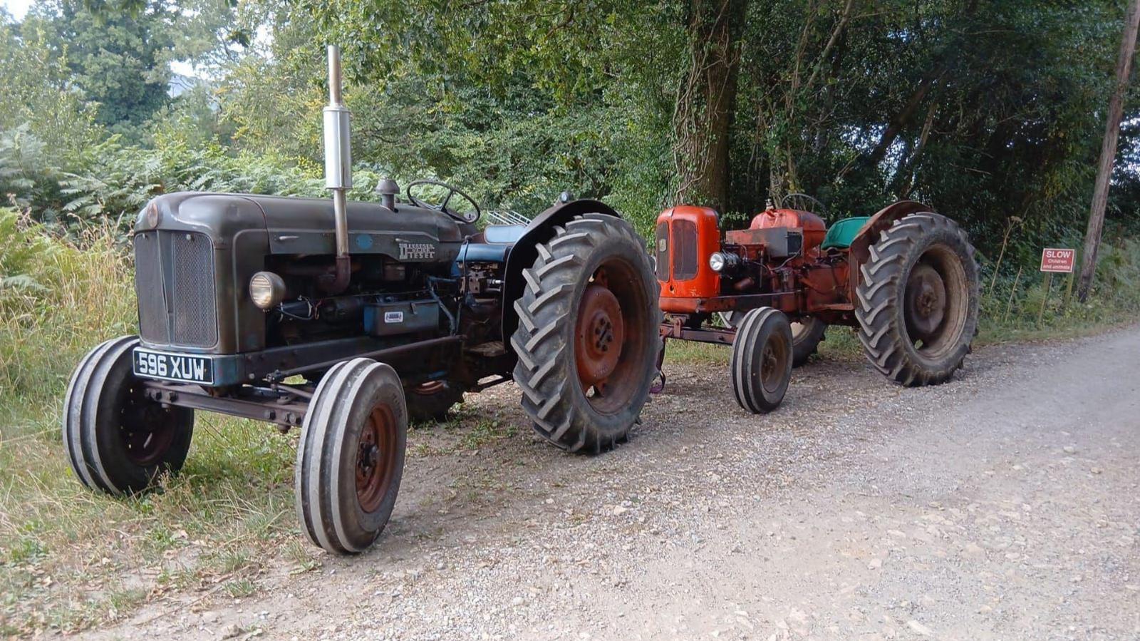A black tractor at the front of the image with a red tractor at the rear.