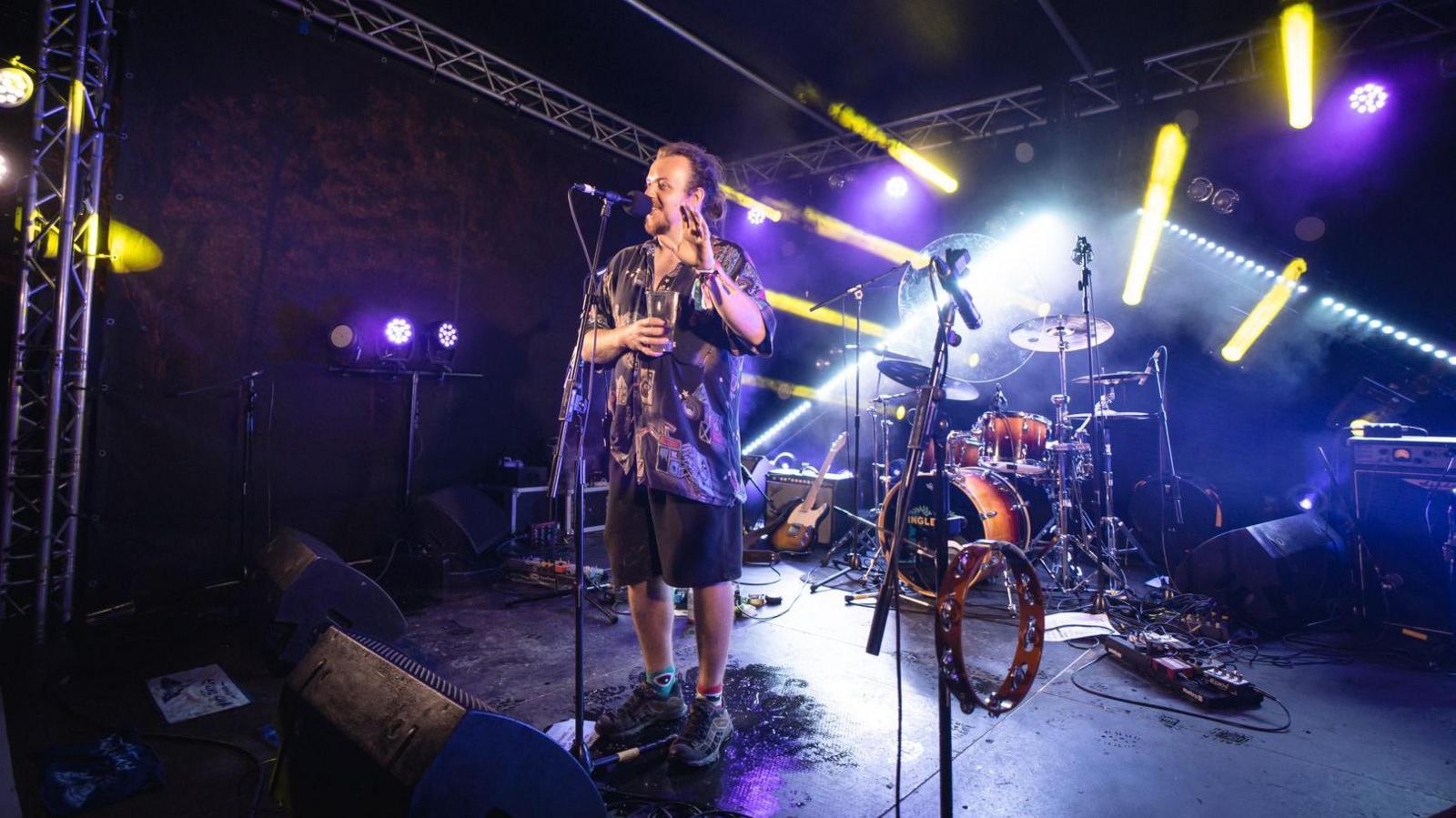 Dom Mosley of Inglefest standing on a stage in from of a drum kit talking into a microphone