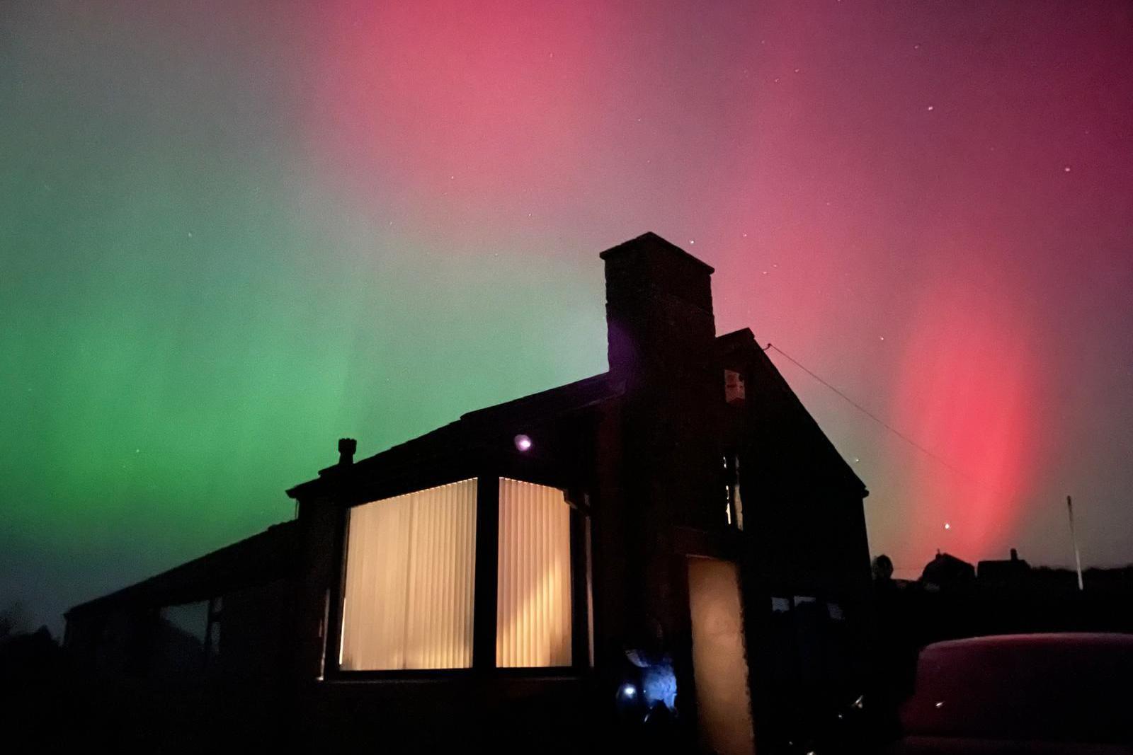 Pink and green Northern Lights over a silhouetted bungalow