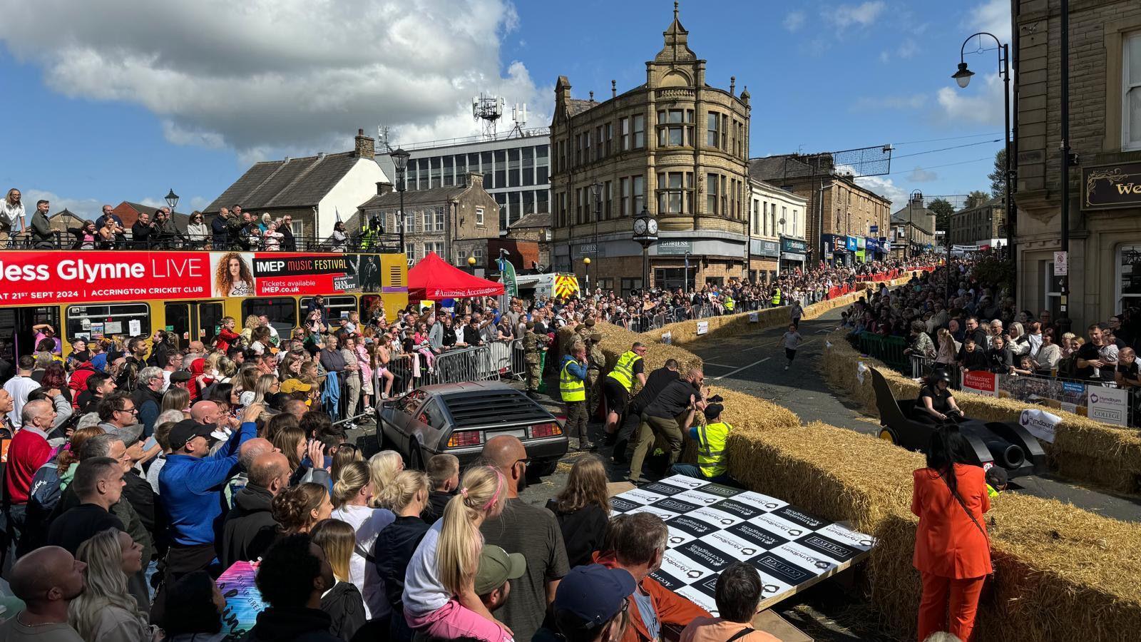 Crowds watch the event in Accrington town centre, with a Delorean car also on show at the side of the racetrack as a black Batman-themed cart goes past. 