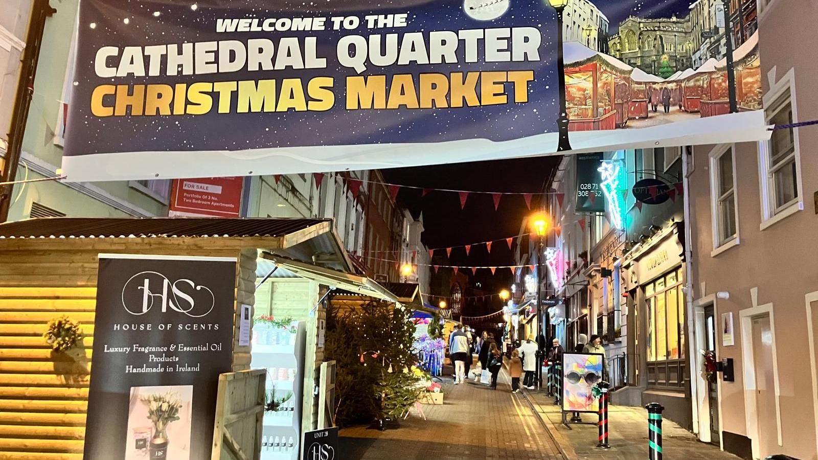 A narrow street with a number of log cabins trading.
A banner can also be seen which reads: 'Welcome to the Cathedral Quarter Christmas Market'