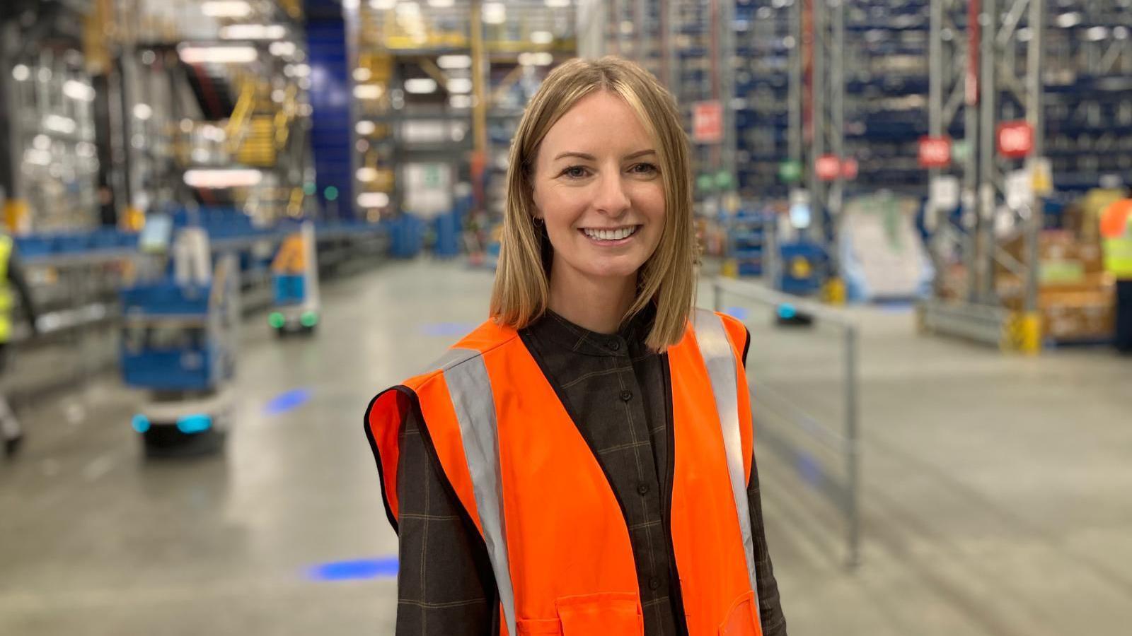 Jenna Whittingham-Ward wearing an orange hi-vis jacket stood in a warehouse