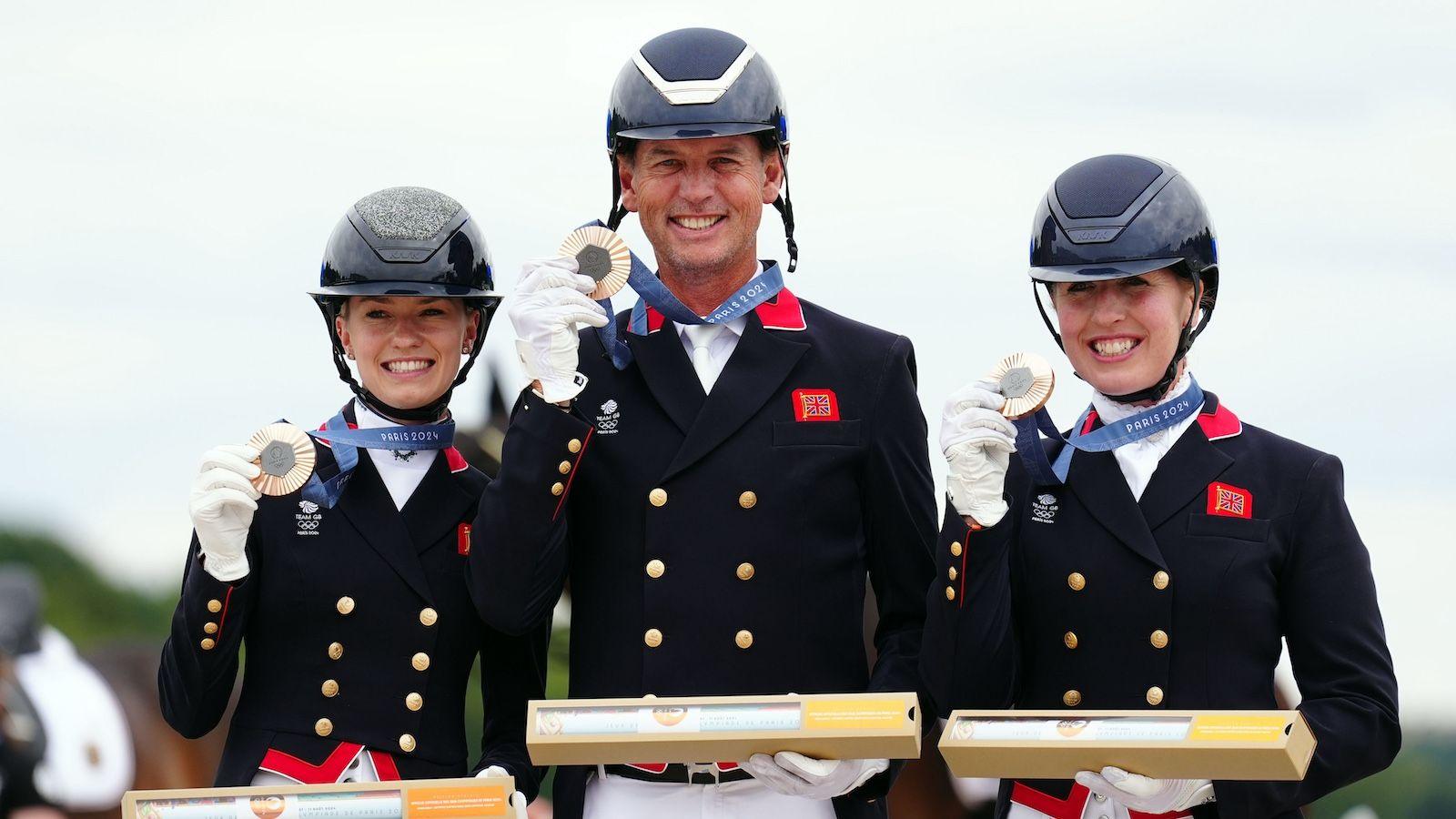 Lottie Fry, Carl Hester and Becky Moody hold up their bronze medals on the podium