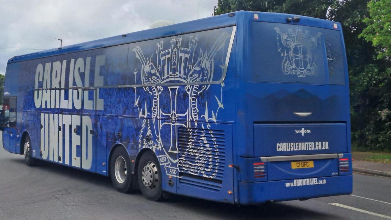A view from the back of a blue coach with 'CARLISLE UNITED' and the club's badge adorned on the left-hand side