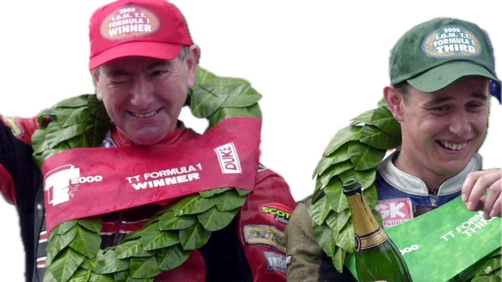 Joey Dunlop in red leathers and cap and John McGuinness in a green cap smiling with garlands around their necks.