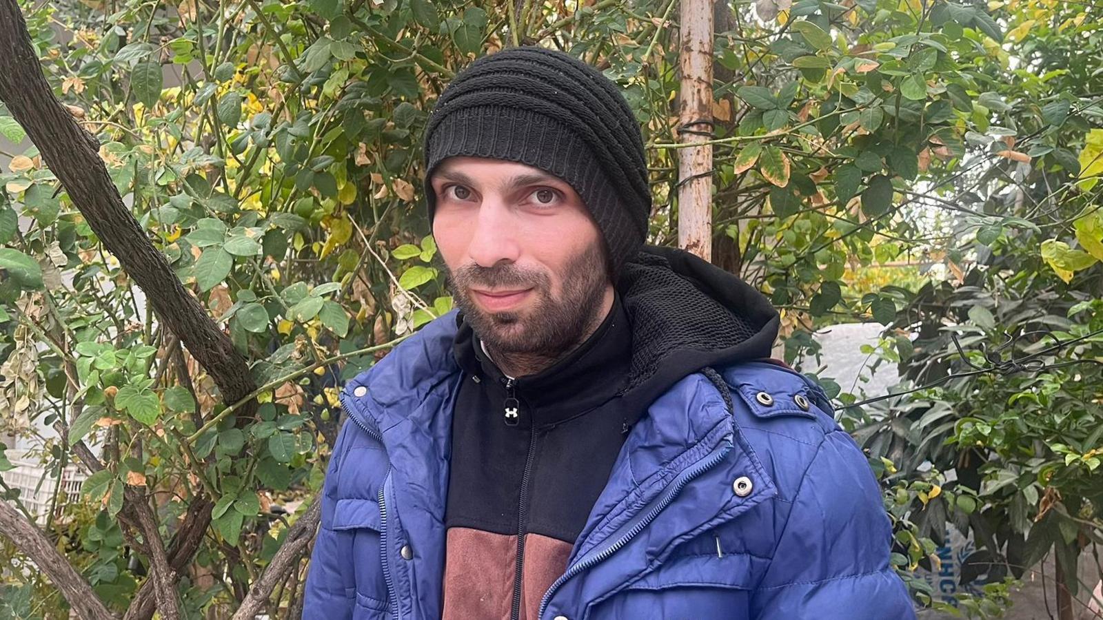 Qasem Sobhi Al-Qabalani wearing a beanie and warm coat smiles against a backdrop of trees