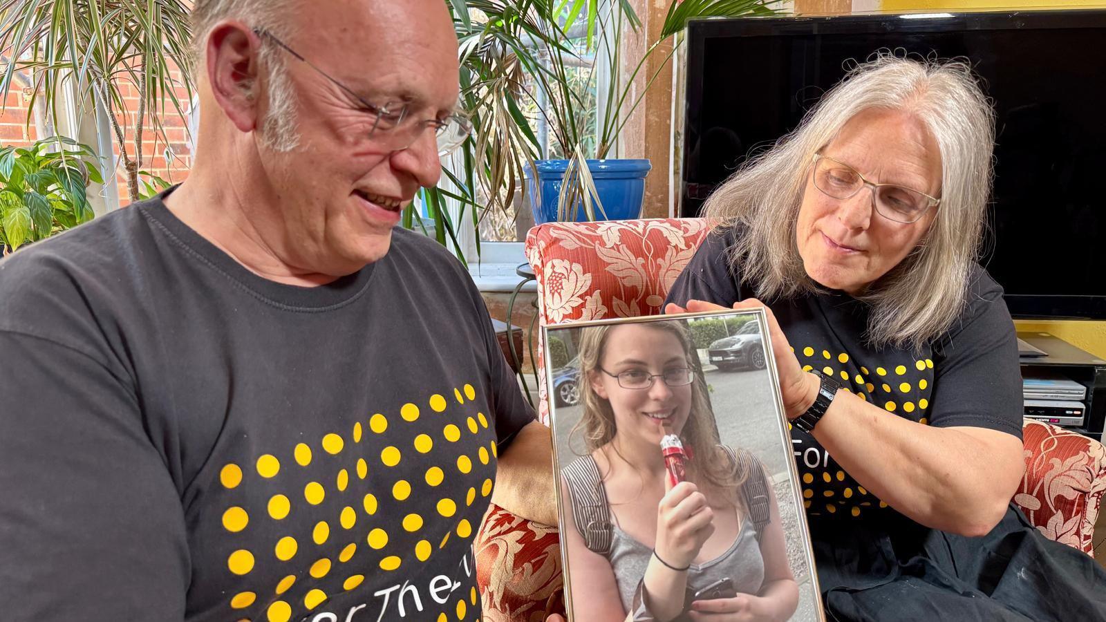 Bob and Maggie Abrahart look at a photo of their daughter, Natasha. They are sitting in their lounge, both on arm chairs.