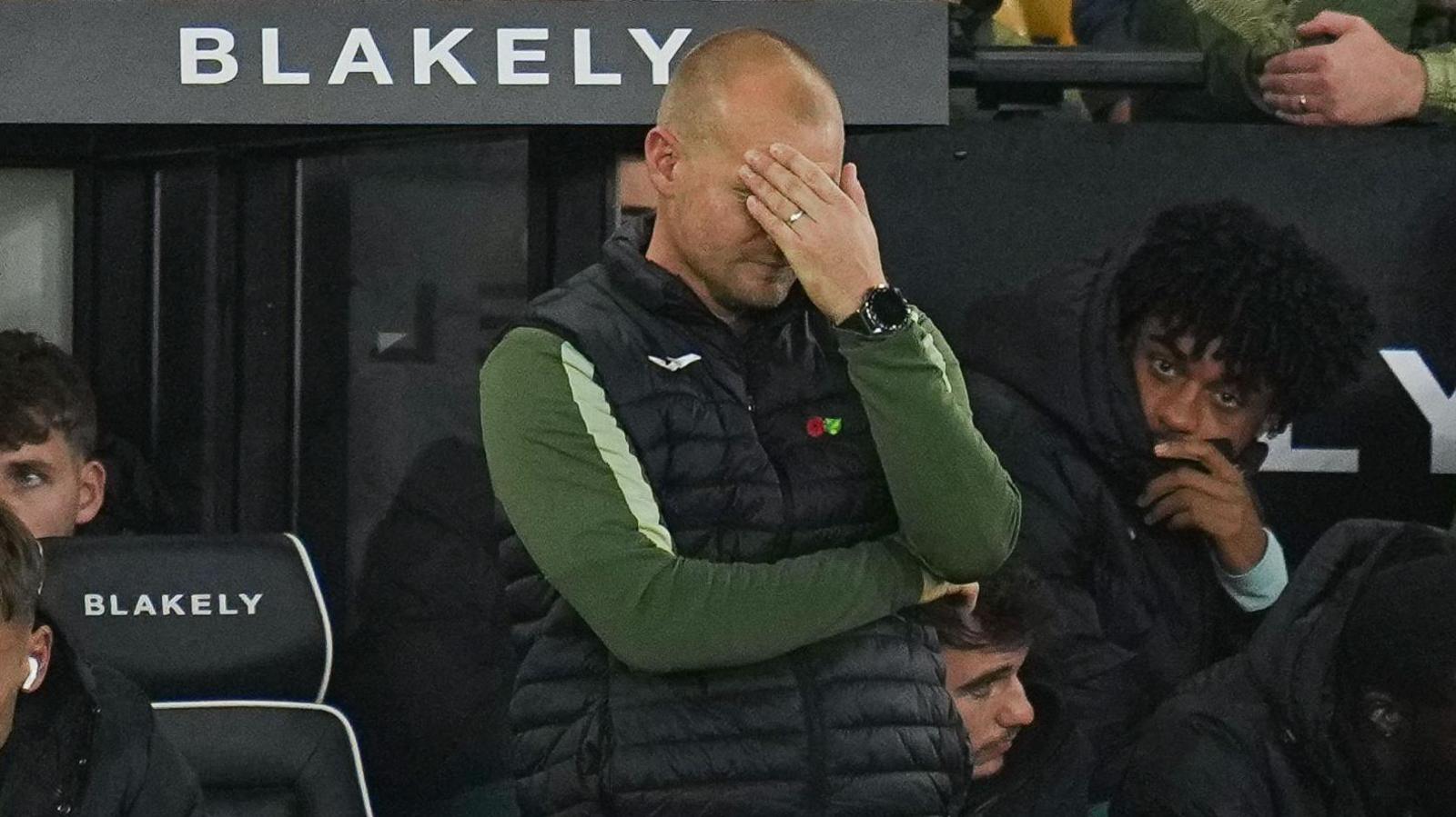 Liam Manning covers his face during defeat to Leicester