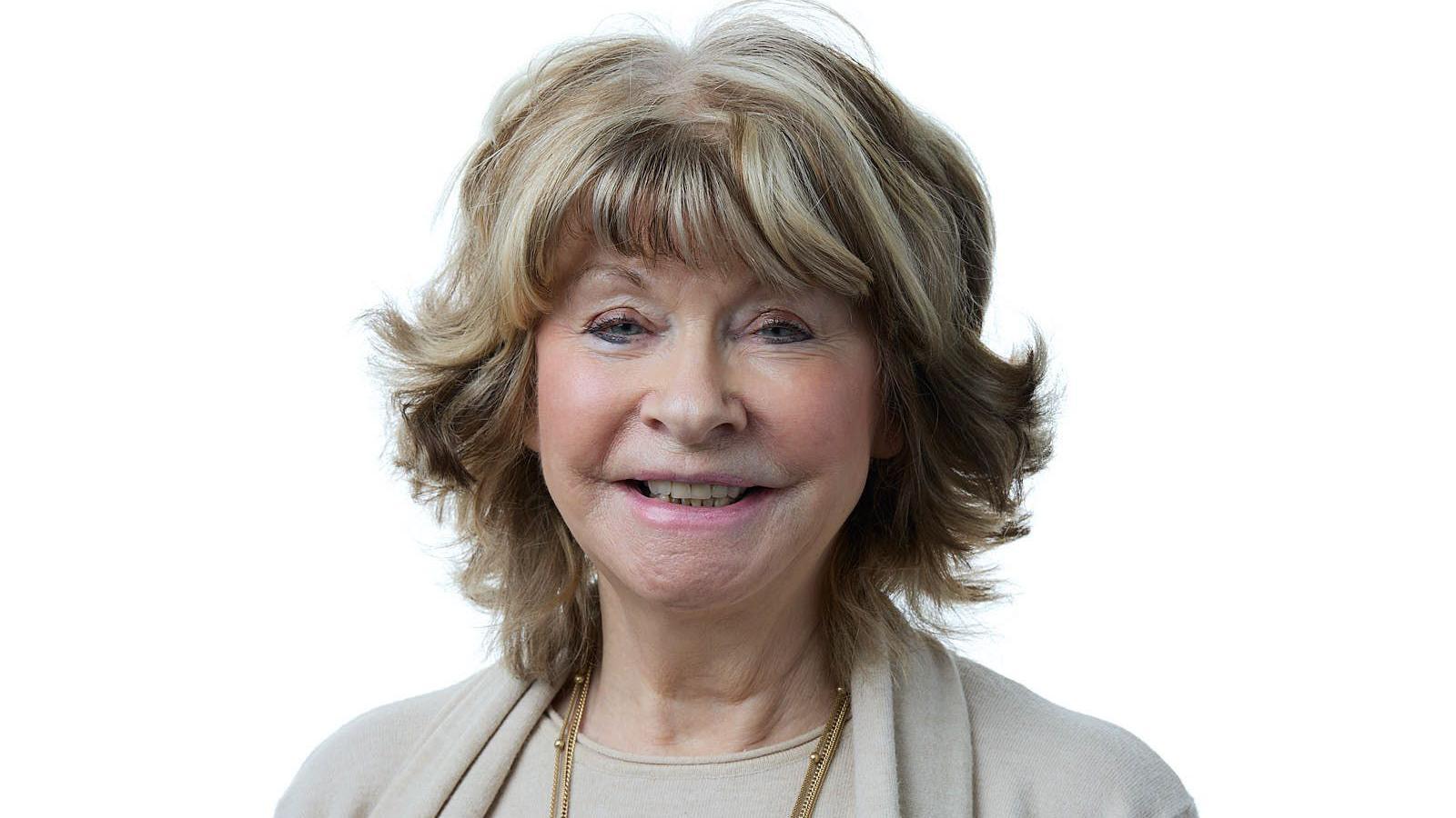 Denise Jeffery smiles at the camera. She has blonde bobbed hair and is wearing a cream-coloured jacket and top, along with a gold necklace.