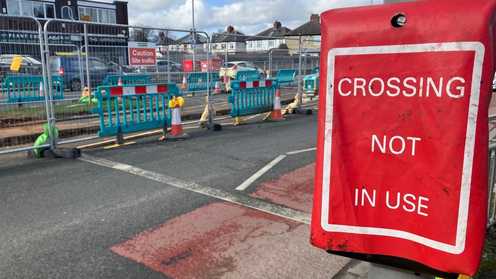 A red sign covers a crossing. It reads "crossing not in use" behind it, blue plastic barriers and metal frames force drivers into single lane traffic.