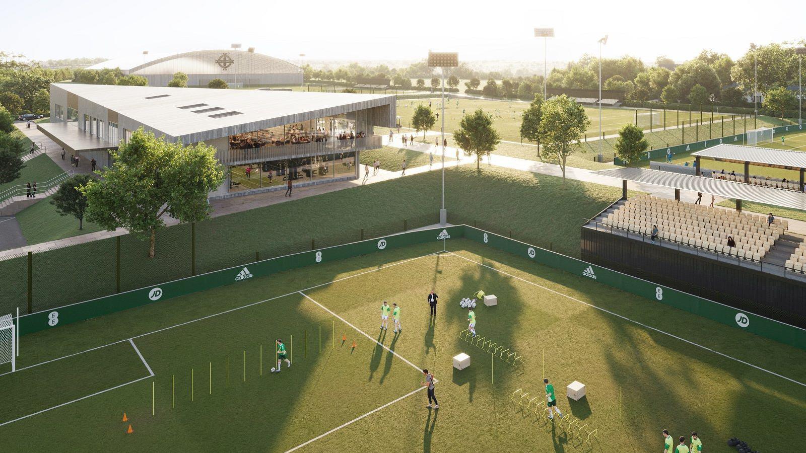 A computer rendering of the proposed IFA training centre which shows a corner of a football pitch being used for training with a small grandstand lining one side. In the background is a building and another football pitch. 