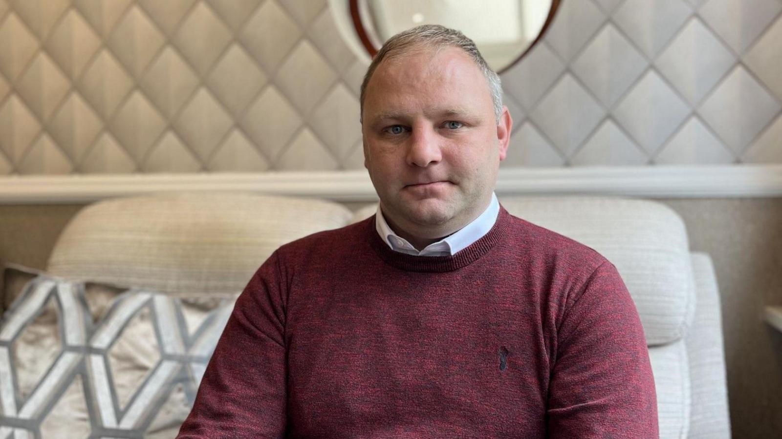 Gareth Jones, in dark red jumper, sits on a sofa