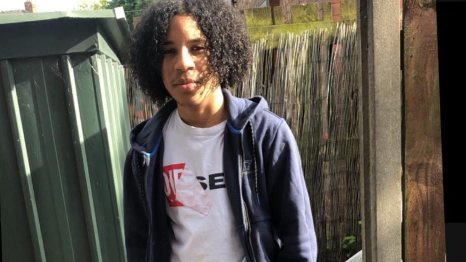 Rhamero West, wearing a white Diesel brand t-shirt under a blue jacket, smiles at the camera in a garden