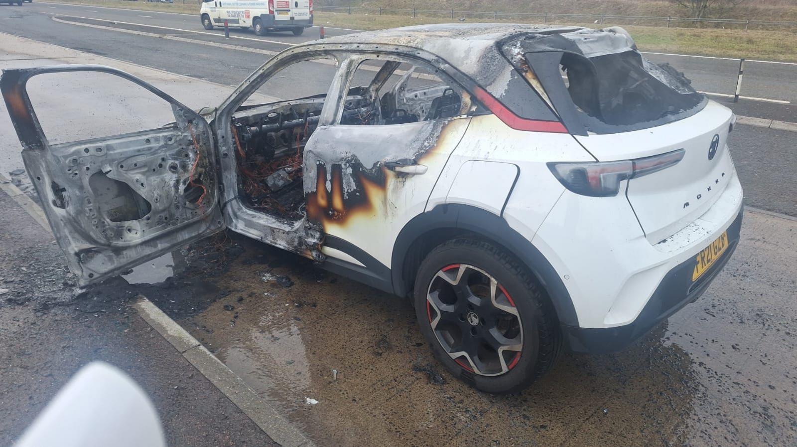 Pamje anësore e makinës së bardhë të dëmtuar plotësisht nga zjarri. Të gjitha dritaret janë hequr dhe ka mbeturina përreth automjetit.