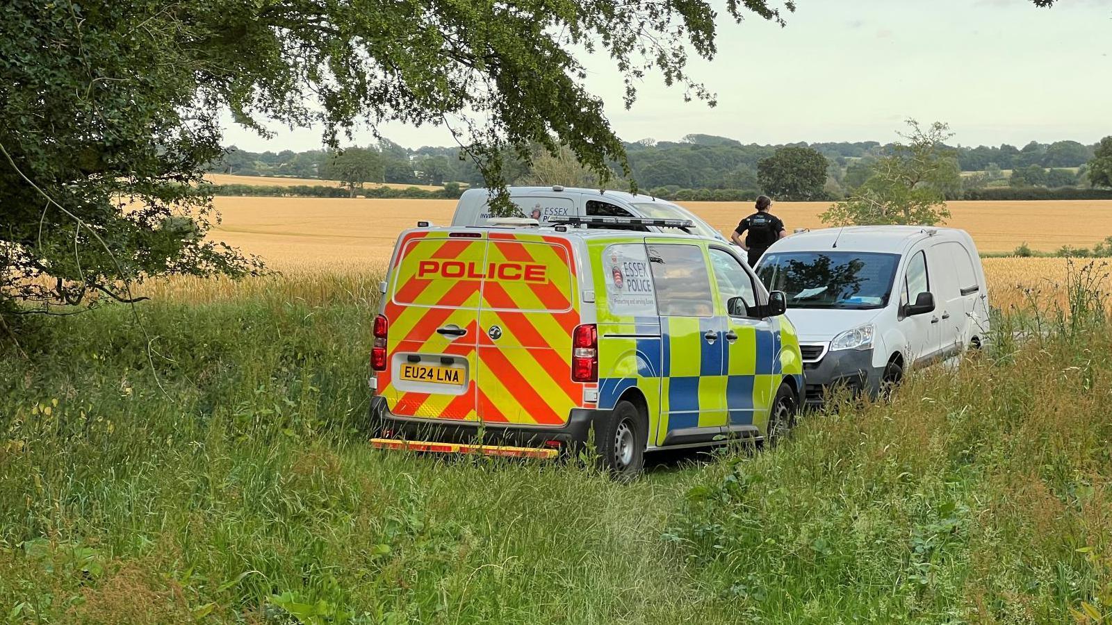 Three police vans parked on a field, with an officer looking away into the field.