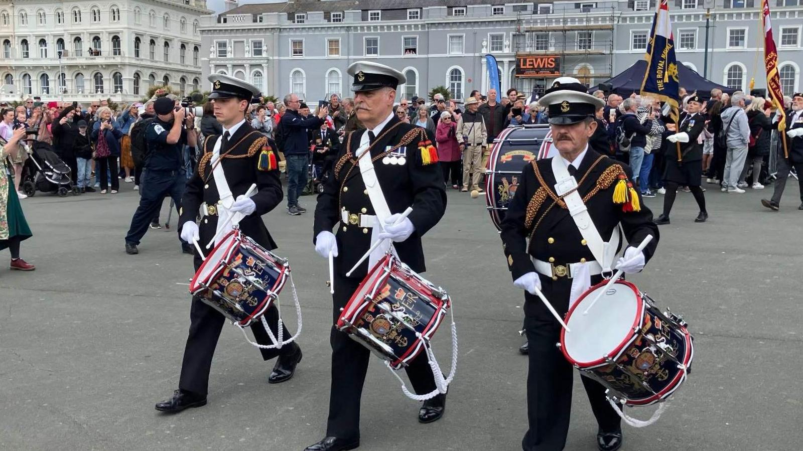 Three men dressed in military regalia holding drums on Plymouth Hoe.