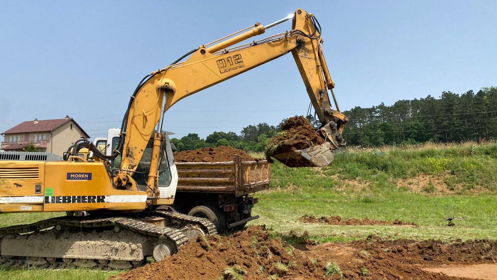 Digger machine digs up soil as the construction of a tennis court gets under way