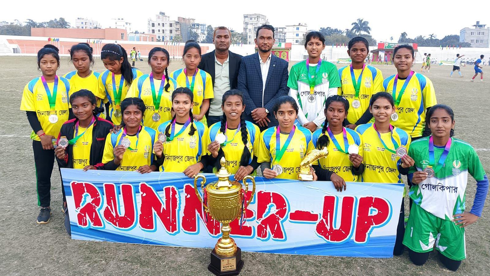 A team of young women in sports gear pose behind a runner-up poster and a gold cup