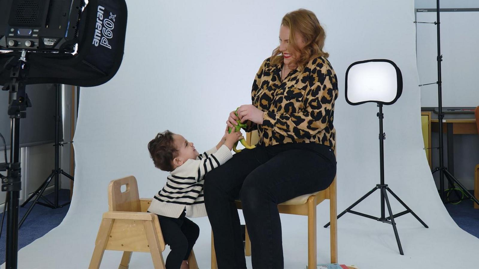 Lauren Somerville and her son Ben sitting on a wooden chairs in a photographer's studio. Ms Somerville is wearing a leopard print top while Ben is wearing a white jumper with black stripes. They are playfully fighting over a child's toy. 