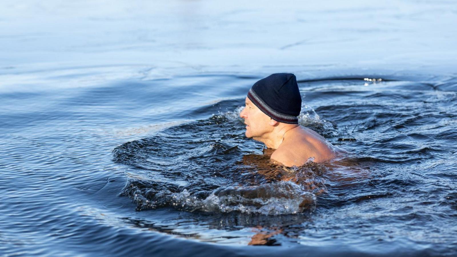 Man wearing a woollen hat swimming in lake. 