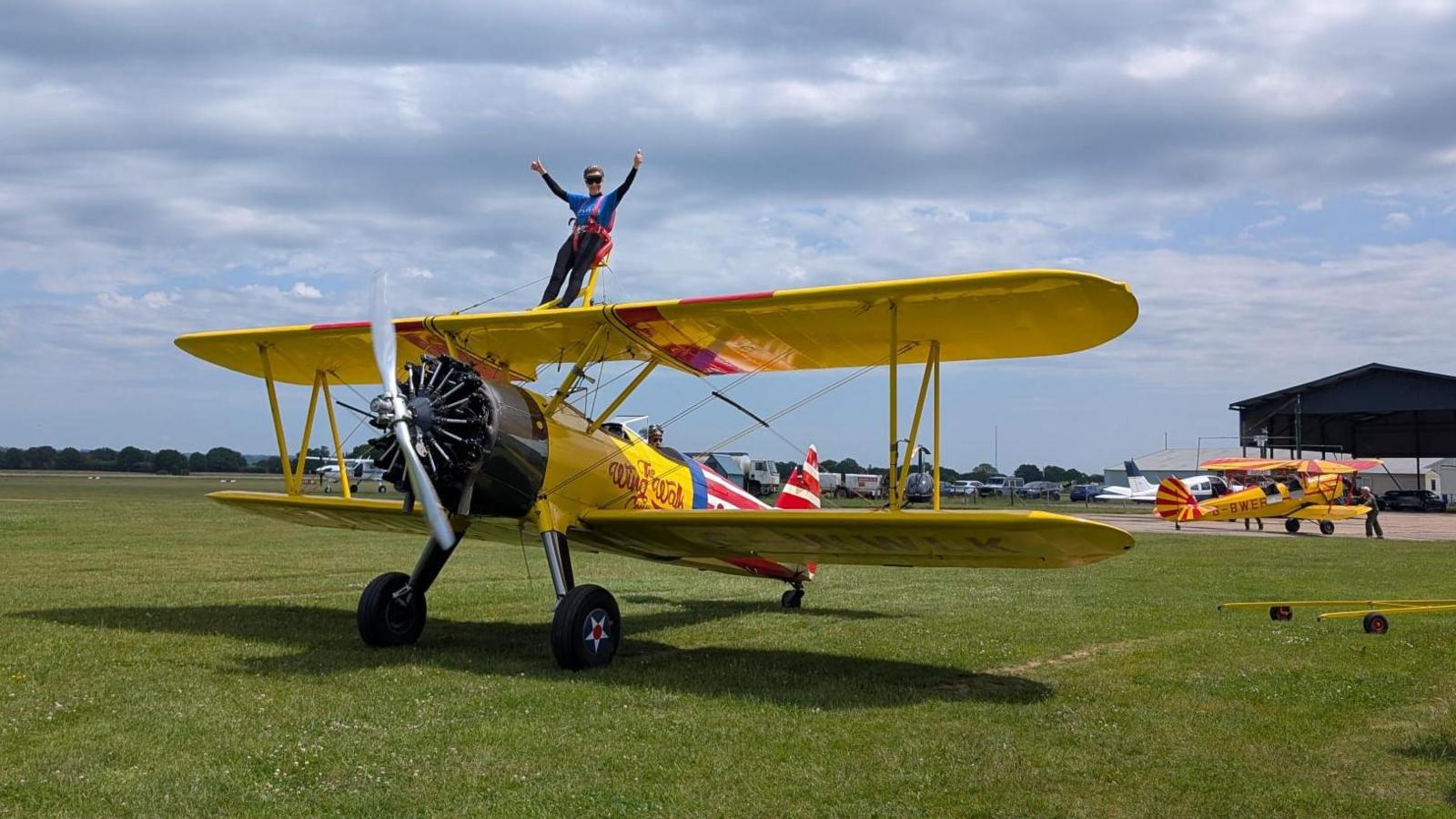 An elderly woman is strapped onto the yellow wings of a plane.