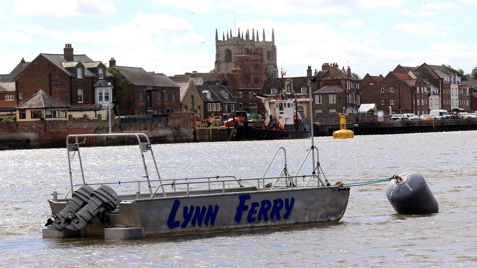 A small metal boat with "Lynn Ferry" written in blue letters sits on the River Great Ouse