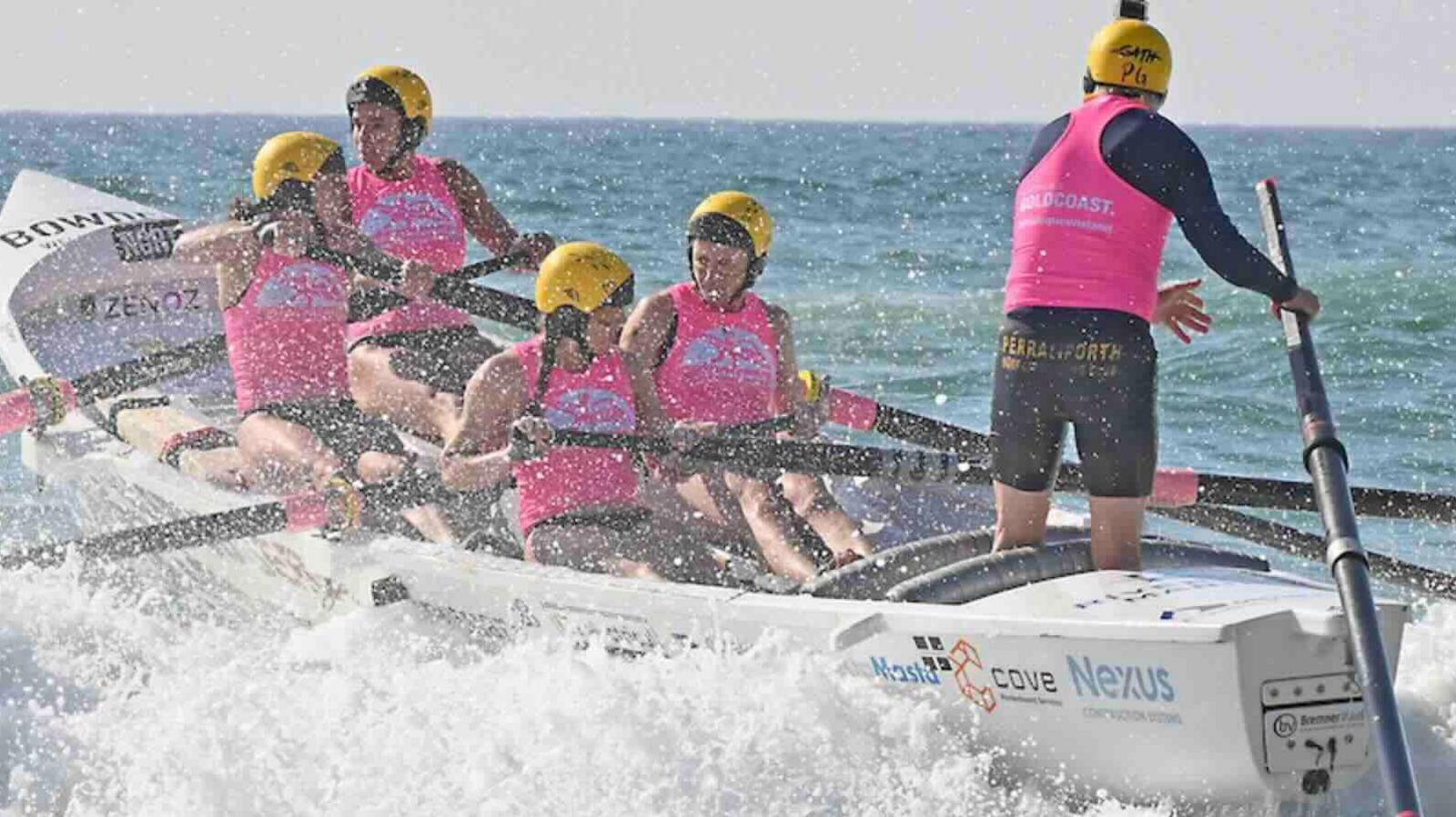 Members of Perranporth Surf Lifesaving Club rowing a boat on choppy water. They are wearing pink lifejackets and yellow helmets