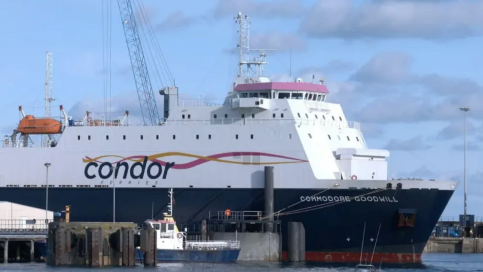 A Condor ferry emerges from the left, with sea seen to the right and Commodore Goodwill written on the side with a blue background on the lower half and a white background beneath the main branding on the top half 