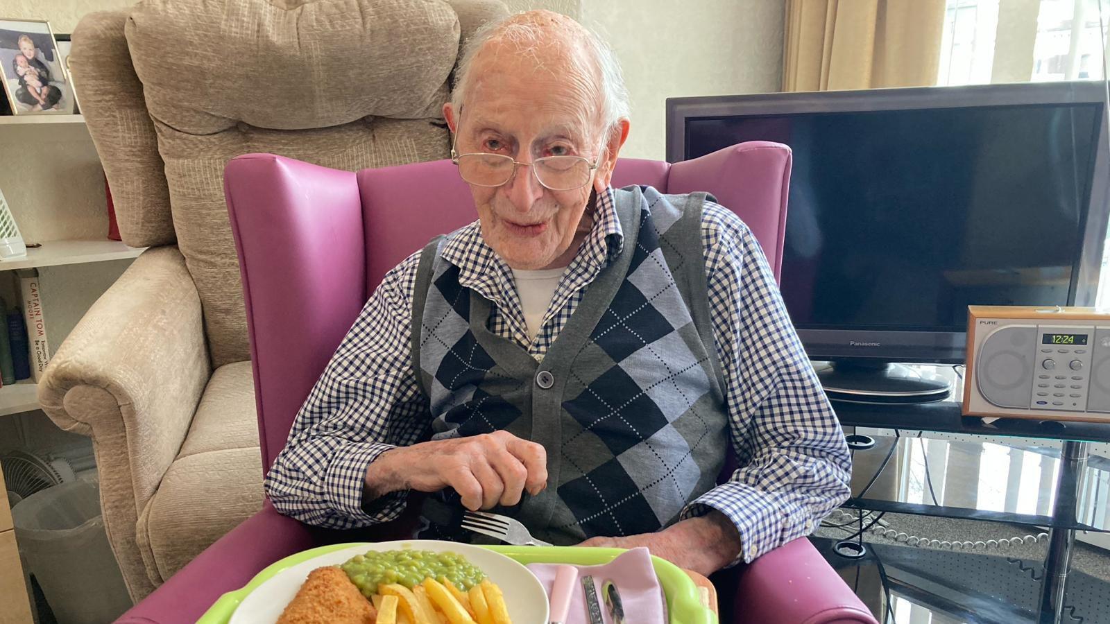 An elderly man sitting down in front of a plate of fish and chips.