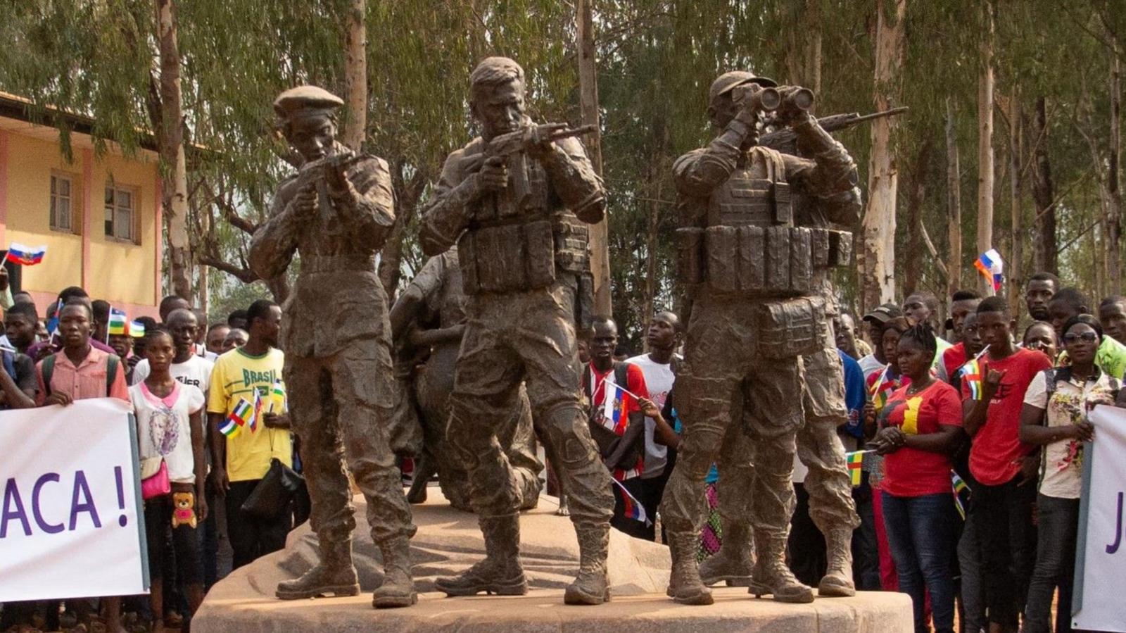 Three statues representing Central African soldiers and Russian armed men protecting a woman and her children. Two are of soldiers holding guns ready to fire while one holding binoculars. A crowd of people surround the statues