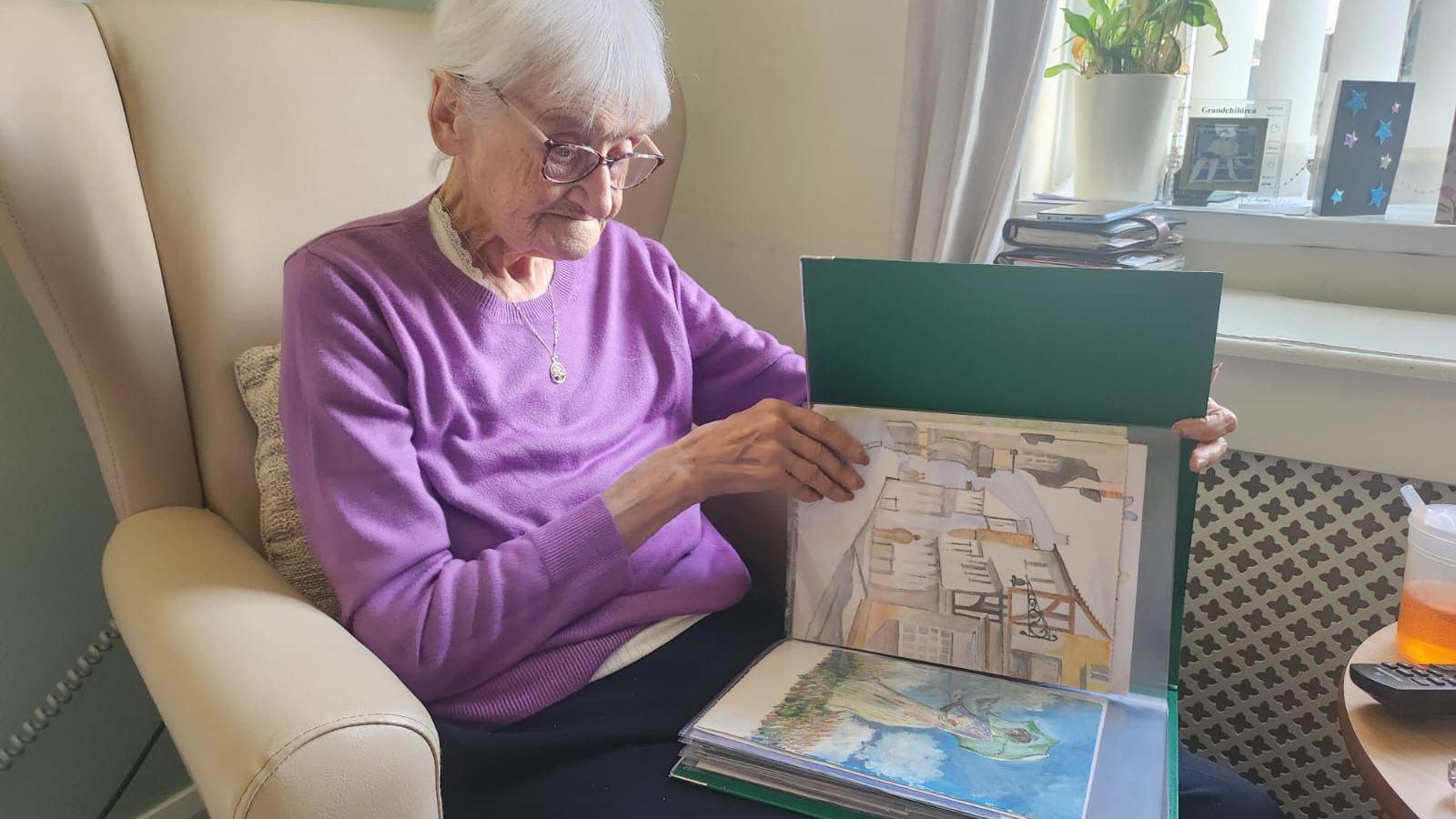 Patricia, wearing a purple jumper, looking through her portfolio of paintings.