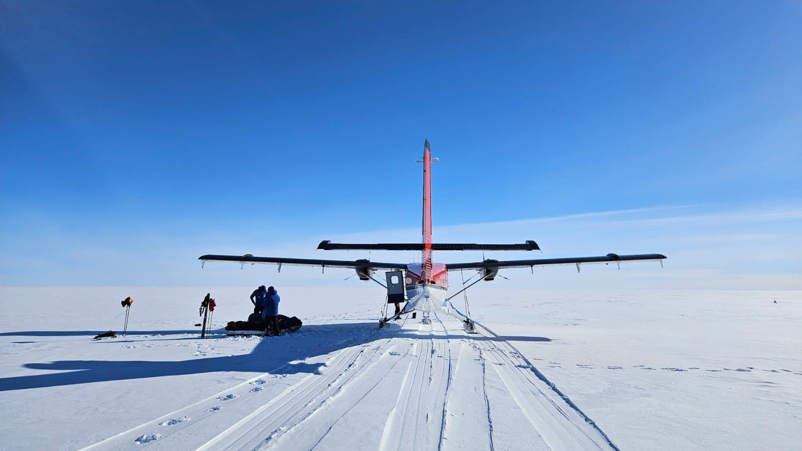 A red and white plane on white snow on a clear day.