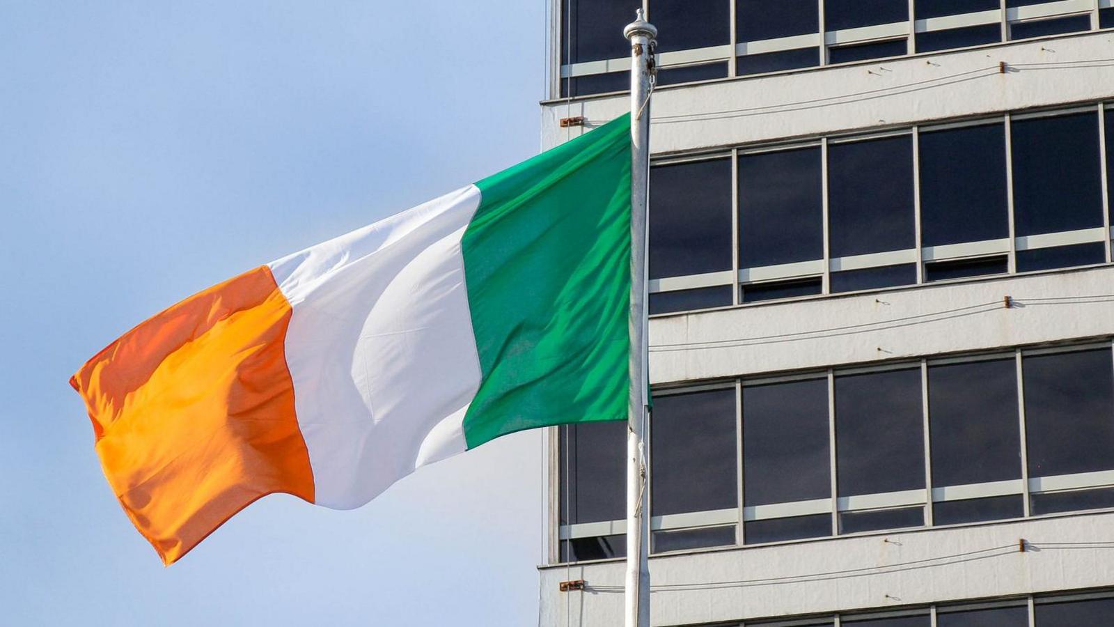 An Irish flag (orange, white and green) colours in front of a buliding.