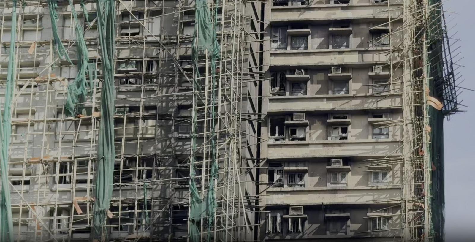 Apartment block with scaffolding that appears to be made of bamboo and green mesh. 
