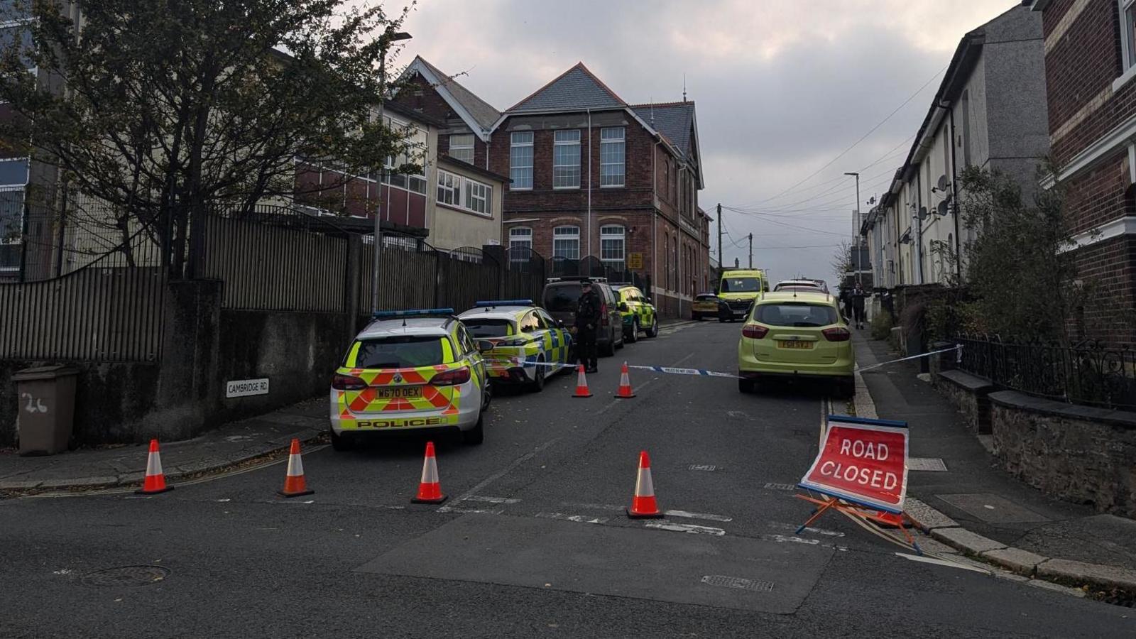 Cambridge Road is closed with traffic cones and a 'Road closed' sign. There are multiple police cars parked along it.