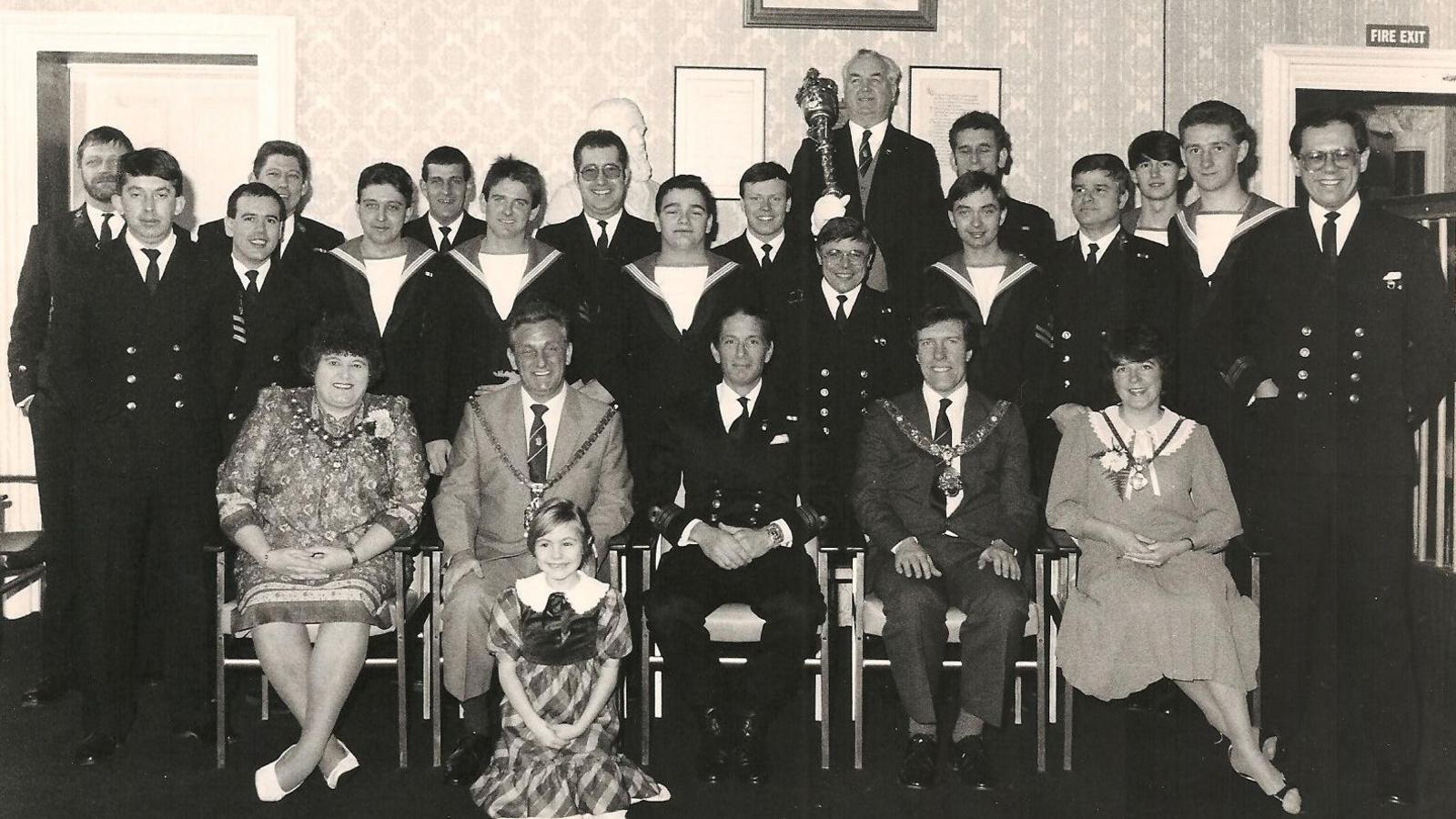A black-and-white photograph taken at Middlesbrough town hall, showing members of the crew led by the Captain Cdr Colin Hamilton with civic dignitaries including Middlesbrough Mayor Malcolm Kirk and Mace Bearer Bernard Martin. The crew are wearing uniforms, while the mayoral party is wearing formalwear and chains.