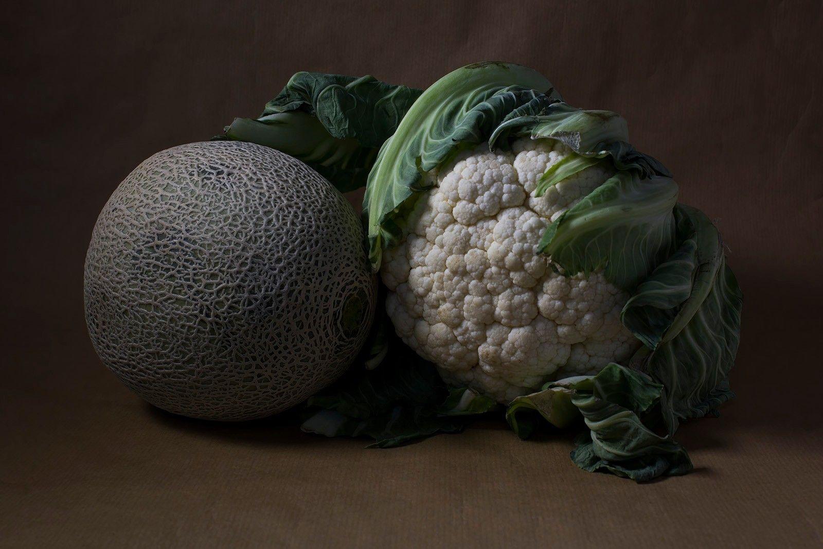 A melon and a cauliflower positioned side by side against a dark background