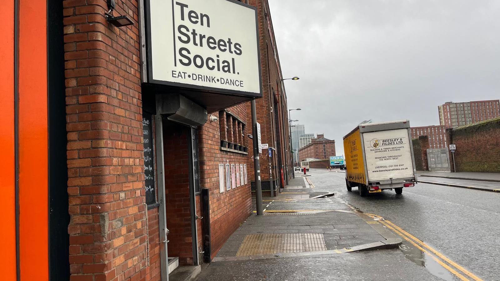 A view down Regent Road in Kirkdale looking towards Liverpool City Centre. A white sign with black lettering reads 'Ten Streets Social. Eat Drink Dance'. 