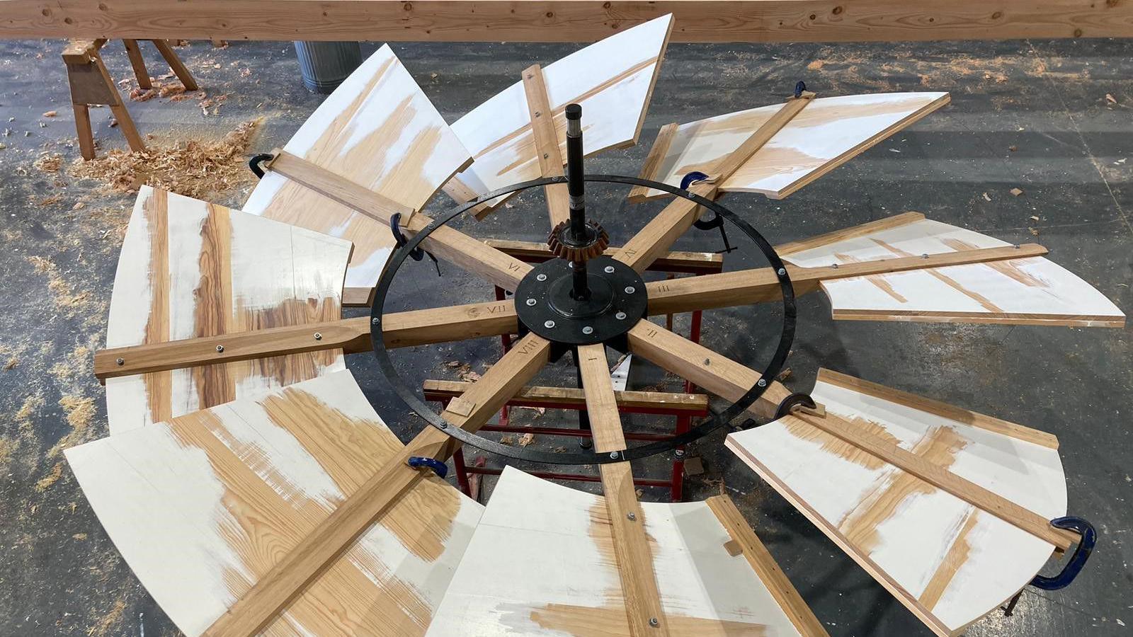 A windmill fantail is pictured in a workshop on the flood. The spiral shaped device has wooden panels fitted to a black metal centre. The panels have some white paint on them.