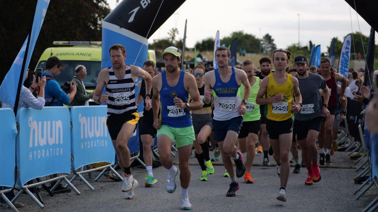 Runners setting off from under an inflatable archway with spectators behind barriers.