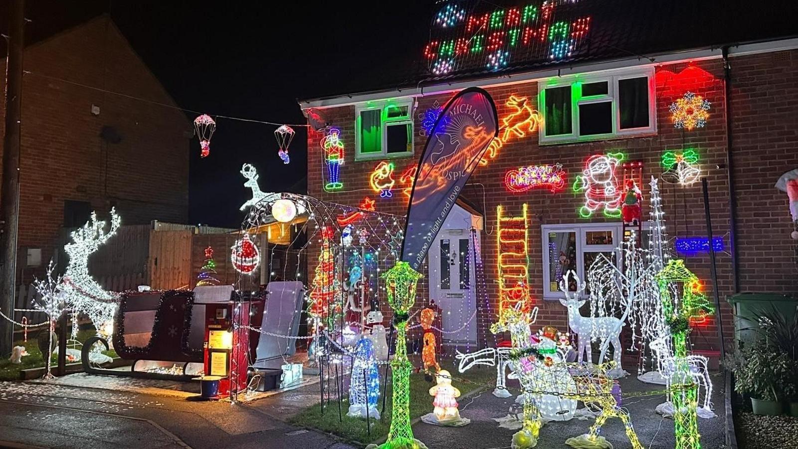 The house is covered with numerous lights and decorations with others in the front of the garden. The decorations include reindeers covered in lights, Santa's sleigh and snowmen.