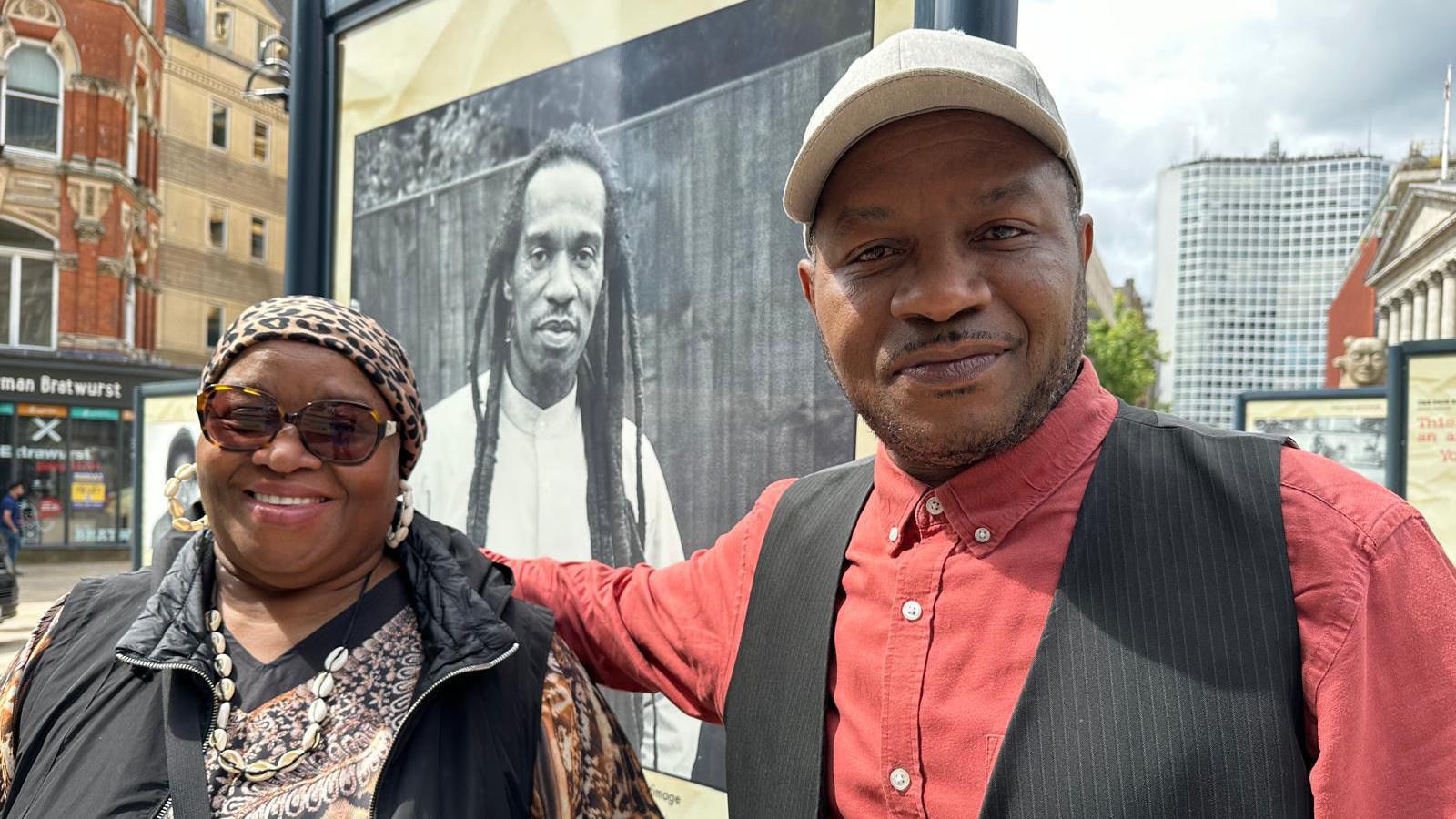 Mr Zepheniah's brother and sister stand in front of a picture of their brother on a street