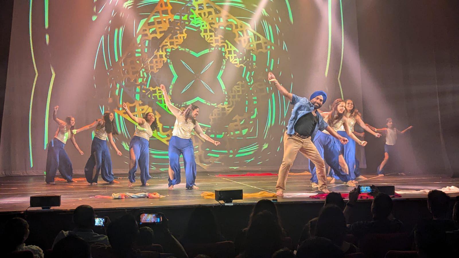 Bollywood dancers on a stage, with a light show in the background. They are dressed in blue and cream coloured clothes.