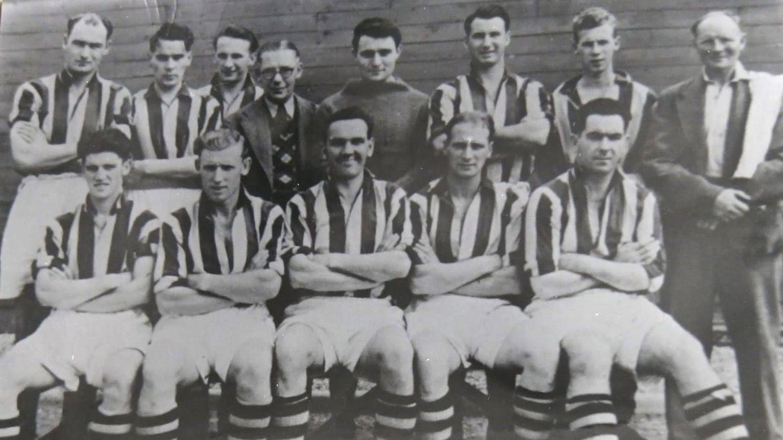 A black and white photo of a football team, its club chairman, and trainer, posing for a team photo. There are five players sitting in the front row, while the other six players, as well as the chairman just left of centre and the trainer on the right, stand behind them. The outfield players wear white-and-dark striped jerseys, with white shorts and hooped socks seemingly of the same colours as the jerseys. The goalkeeper wears a dark top, while the chairman, who has glasses, wears a suit, tie and a patterned waistcoat. The trainer on the right wears a dark jacket and trousers, a white shirt with no tie, and has a towel over his left shoulder.