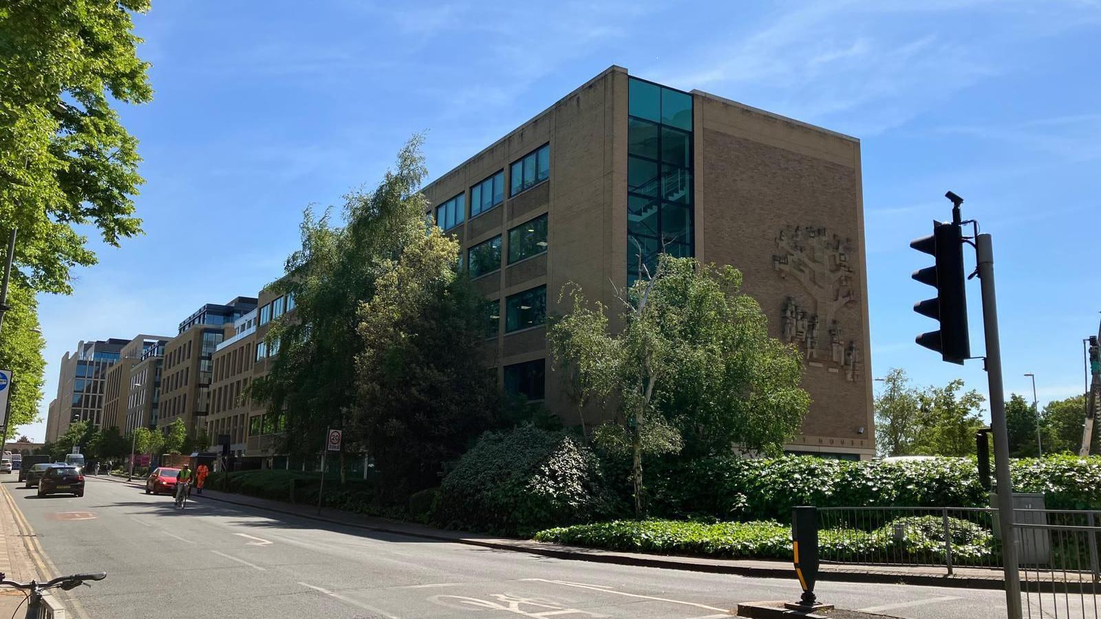 Street view of the building on a sunny day. The sculpture can be seen on the side of the building, but not from the front. 