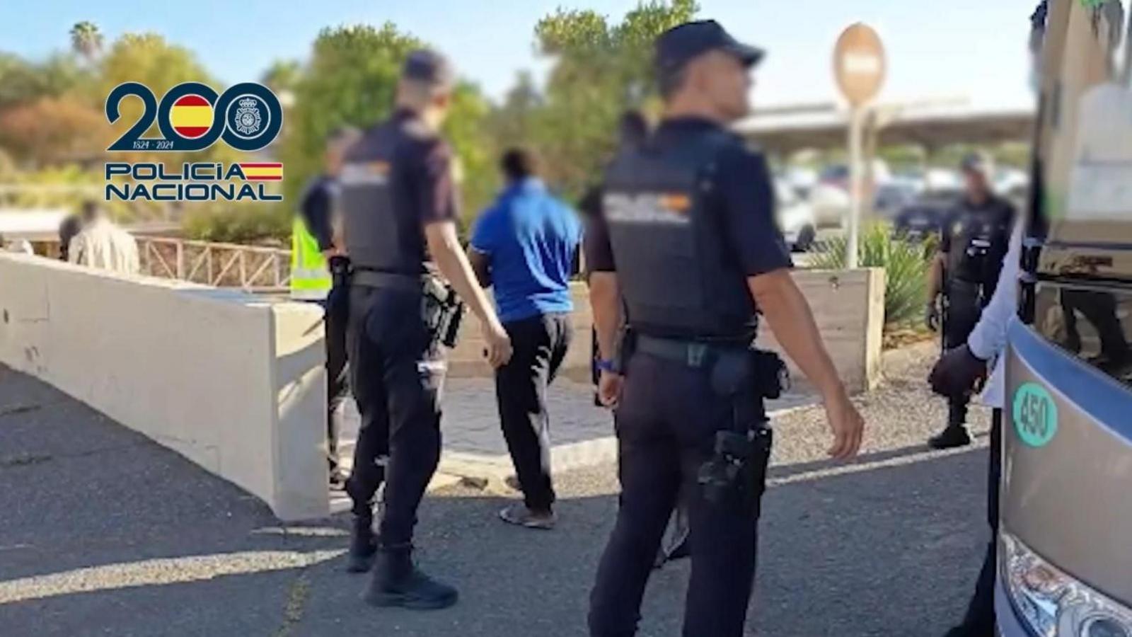 A police handout photo showing the backs of police with their faces blurred, standing next to a coach as people from the migrant boat exit it.