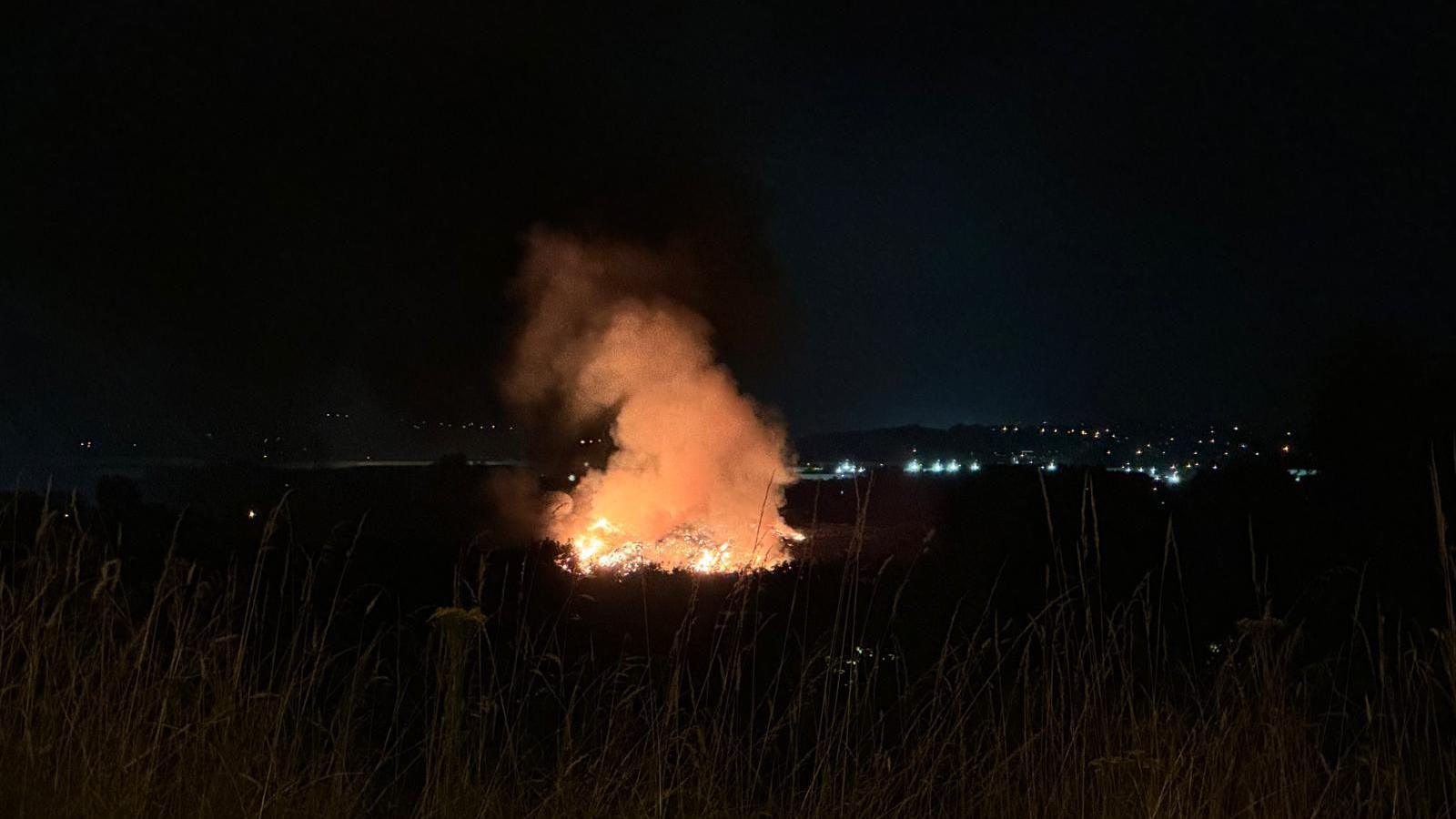 A large fire at night time, with the lights of a town visible in the background