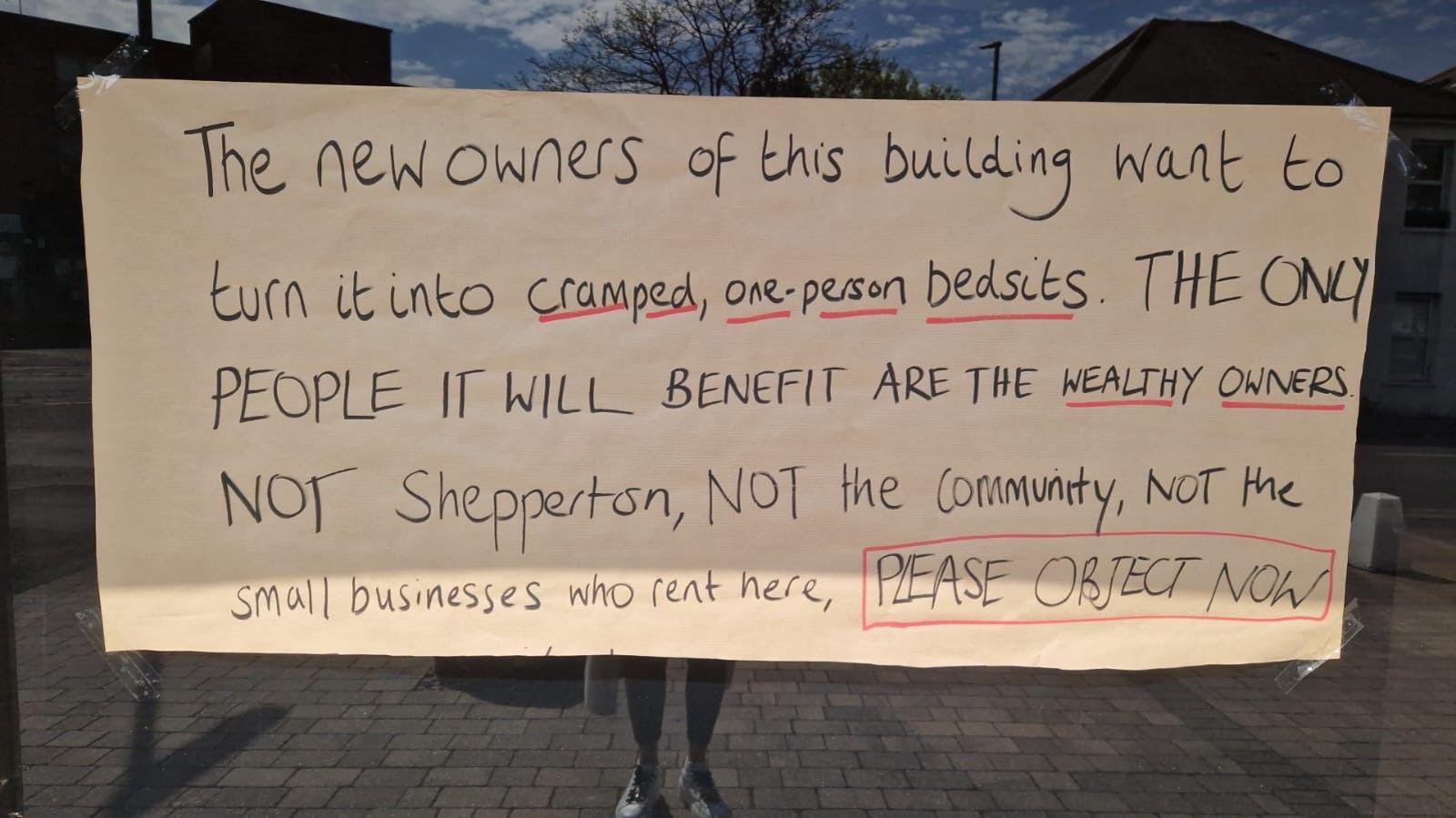 A handwritten sign in a window. It reads "The new owners of this building want to turn it into cramped, one-person bedsits. THE ONLY PEOPLE IT WILL BENEFIR ARE THE WEALTHY OWNERS NOT Shepperton, NOT the community, NOT the small businesses who rent here, PLEASE OBJETC NOW".