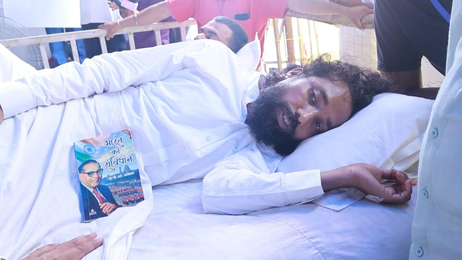 Devendra Nath Mahto wearing a white tunic, is seen laying down at the protest site with a copy of the Indian constitution kept near him 