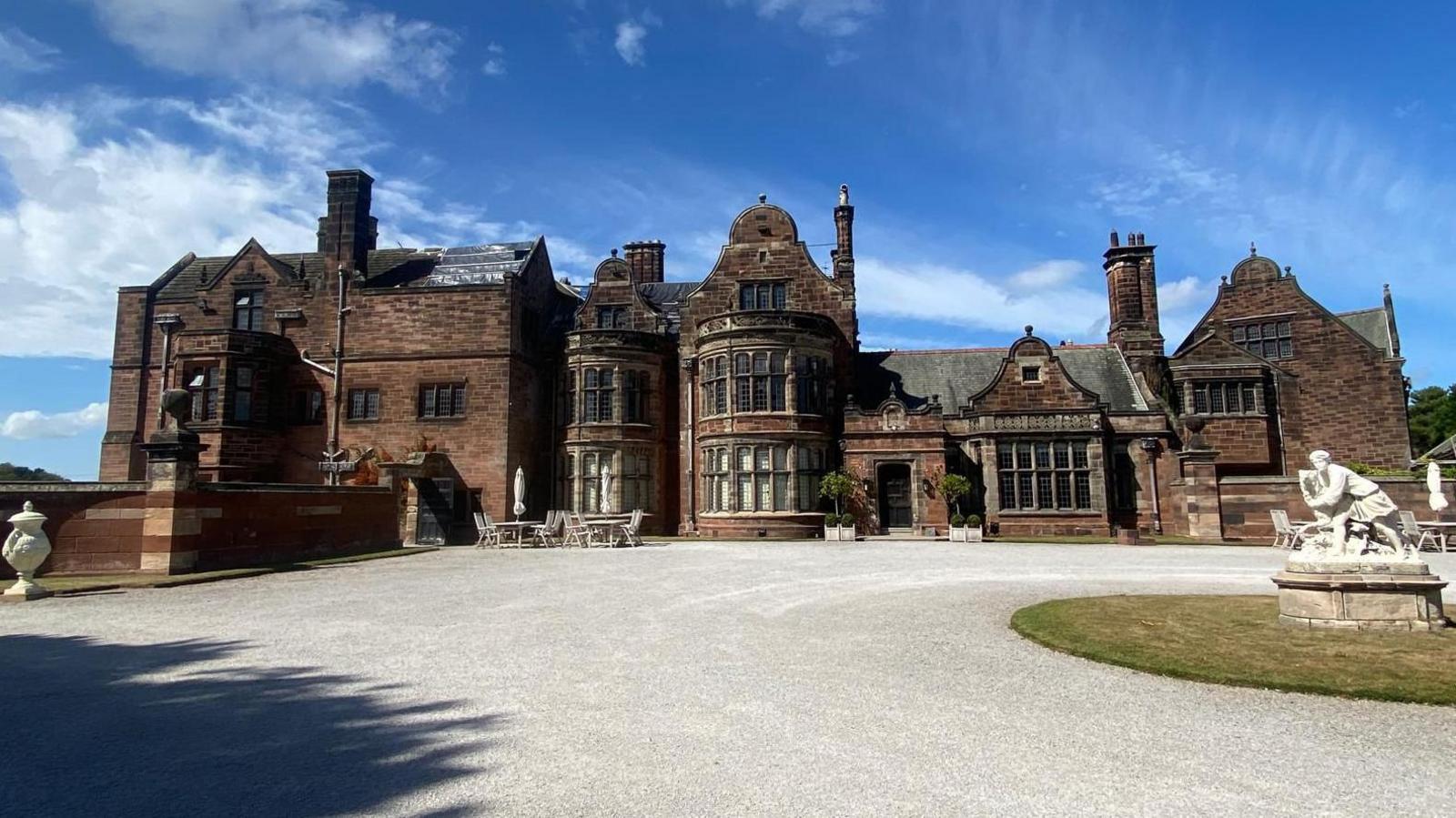 A huge dark brick manor house at the end of a gravel driveway.